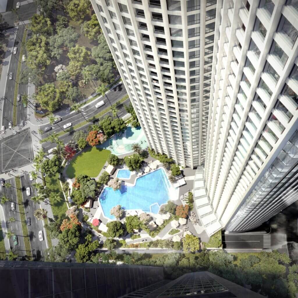 High-angle aerial view of curved white skyscraper overlooking blue swimming pool and landscaped gardens.