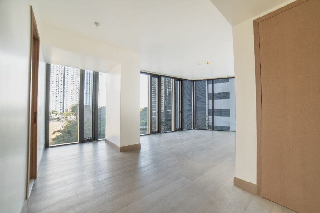 Spacious, empty master bedroom with light wood flooring and floor-to-ceiling windows showing urban views.