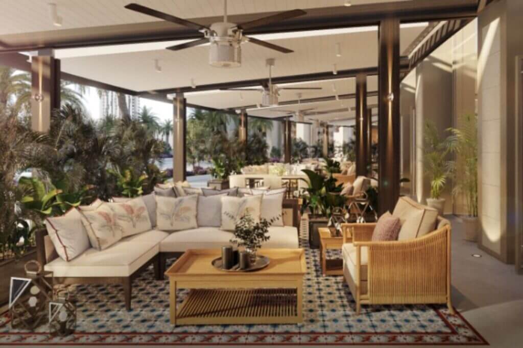 Covered outdoor lounge area with white sectional sofas, wooden coffee table, and ceiling fans amidst tropical greenery.