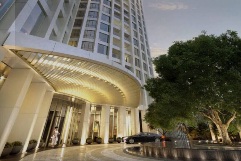 Low-angle view of a luxury building entrance featuring a curved white canopy and illuminated columns at dusk.