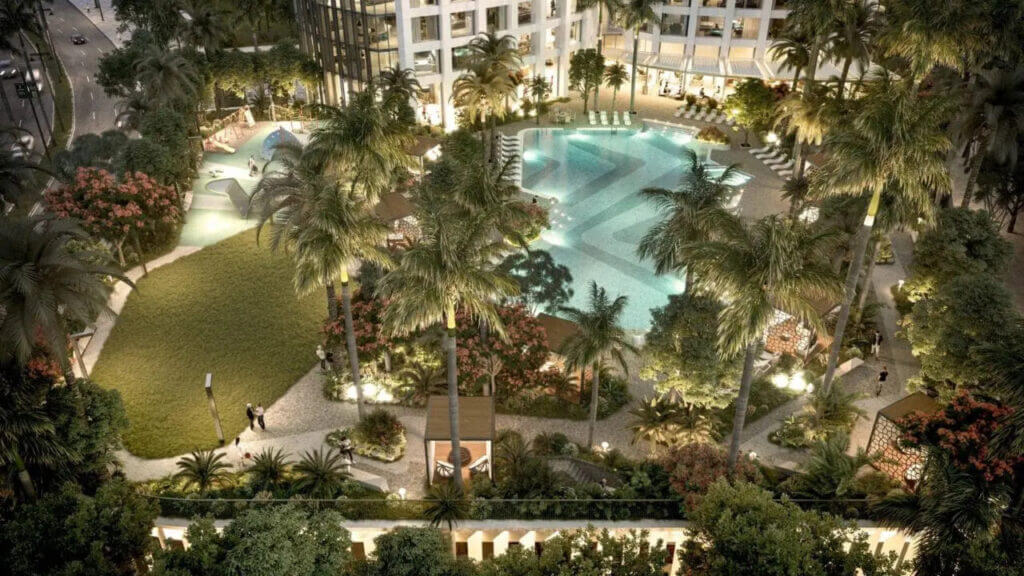 Aerial view of a resort-style swimming pool surrounded by palm trees and landscaped gardens in a residential complex.