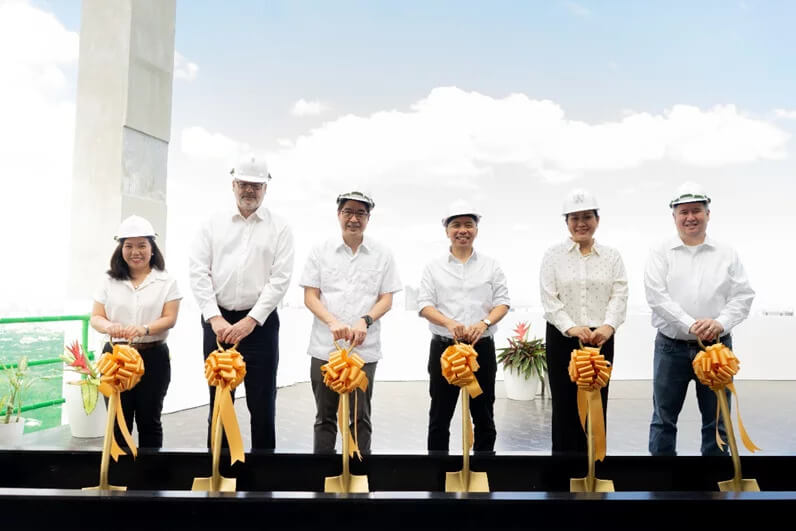 Four men in white shirts and hard hats standing at a topping-off ceremony with golden shovels and ribbons.